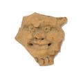 Round clay plaque depicting a face with a broad nose and bulging eyes, cheeks and forehead. The plaque is fragmentary and only a small part of the hair and the beard can still be seen. Considering the evil facial expression, this is probably a representation of a demon. The plaque was most likely used as an appliqu for a vessel. For an almost identical object see MAS.105;