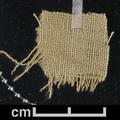 Fragment of buff/yellowish woven (tabby) textile.
