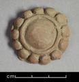 Round ornament made of red clay with a white slip. The ornament represents a jewel and consists of a bigger stone in the centre set within a plain band and a bead border. It was most likely part of a BodhisattvaԳ attire.