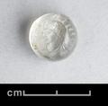 Round seal made of intaglio rock crystal. The decoration shows a beardless male person in three-quarter profile. The hair is brushed from the centre of the head and forms a heavy bandeau over forehead and ears which is tied with a fillet. The man wears a bead earring and a plain tunic laced in the front. On either side of the head, three Br_hm_ characters have been incised.