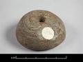 Wooden spindle whorl. The round object is flat on one side and pierced vertically.