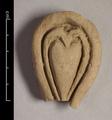 Fragment of wall-decoration made of yellowish clay. The object is pear-shaped with one oval and one heart-shaped incision. Most likely a lotus-petal is depicted here.
