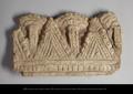 Fragment of a relief ornament representing a textile valance with a horizontal band on top and triangular draperies and narrow tassels hanging from it. Modelled in stucco and still bearing traces of red paint.;