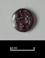 Circular seal made of intaglio garnet. The design is executed in a very simple way and shows a seated female figure in side view. She has long hair and wears a long garment.