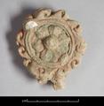 Round stucco ornament. In the centre is a six-petalled flower with a prominent boss. It is surrounded by a double-ring border to which curling flames are attached. Traces of green and red pigments remain.