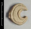 Fragment of wall-decoration (?) made of light grey clay with traces of red paint. The crescent-shaped object is decorated with two incised lines.