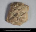 Fragmentary clay figure depicting a lion's face. The animal is shown in full frontal view with its head surrounded by the mane. Eyes, cheeks and forehead are bulging, giving the lion an evil expression. The fact that the plaque is flat on the reverse side suggests that it was applied to another object, probably a vessel.;