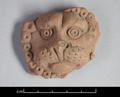 Fragmentary round clay figure depicting a lion's face. The animal is shown in full frontal view with its head surrounded by the mane. The representation is very stylised. The fact that the figure is flat on the reverse side suggests that it was applied to another object, probably a vessel.;