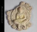 Fragmented plaque made of clay. In the middle of the originally round plaque is a representation of the Buddha sitting crosslegged in meditation pose with the hands folded in the lap. His head is surrounded by a nimbus and he is seated against a mandorla consisting of several layers of either plain rings or a wave-pattern. The mandorla is sourrounded by a a row of lotus-leaves. Traces of yellow pigments, which were used to colour the robe of the Buddha, still remain.