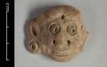 Round clay plaque depicting a human face in full frontal view. The face is very broad with bulging eyes, flared nostrils and short rounded ears which are adorned with earrings. The fact that the figure is flat on the reverse side suggests that it  was applied to another object, probably a vessel.;
