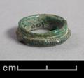 Bronze ring. The outside is ribbed and adorned with a raised band decorated with incised lines. The ends of the band are flattened at the juncture. The ring has a green patine in some places.