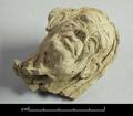 Stucco figure in the shape of the head of an old woman with a grotesque face. Forehead and cheeks are extremely wrinkled and with the bulging brows and prominent cheeks the eyes seem very deep-set. The hair is parted in the middle and brushed back behind the ears.