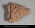 Sherd of a clay vessel. Part of the decoration of this mould-made vessel is still visible. It consists of one half of a palmette motif.