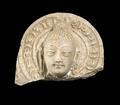 Fragment of a relief plaque made of white stucco. Depicted is the head of a Buddha with elongated earlobes and the clearly visible protuberance (ushnisha). The head is shown against a round halo consisting of several layers, the outermost being a lotus garland.;