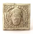 Stucco tile. The square tile shows the head of a Bodhisattva wearing flower-shaped earrings. His hair is parted from the centre and drawn loosely back under a fillet made of alternating plain and beaded bands. It is fastened in a fan-shaped topknot, decorated by a rosette in the centre. The head is surrounded by a circular halo with a beaded border. The figure is modelled in half relief.;