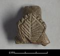 Fragment of a handle made of dark brown clay. It is decorated with a lozenge-shaped appliqu that is adorned with incised lines, imitating the look of a palm-leaf.