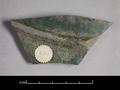 Body sherd of a wheel-thrown vessel made of grey clay. The outside is covered with a dark green glaze and decorated with a horizontal ridge.