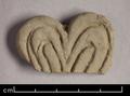 Fragment of a floral ornament made of moulded brown clay, possibly once depicting a stalk. The only part that remains is the upper part of a heart-shaped form decorated with two deeply incised lines. For a larger fragment that was probably made using the same mould see MAS.294.