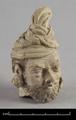 Stucco head of a bearded man with a turban round his head. The left ear is missing, the right one decorated with a an earring in the shape of a large rosette. Traces of dark brown pigments were used to colour hair and beard.
